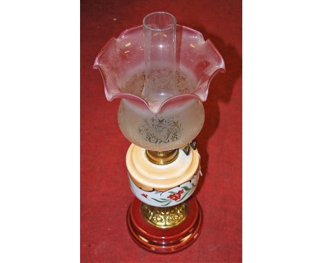 A late Victorian pedestal oil lamp having pink tinted etched glass shade above painted glass reservoir and ceramic base