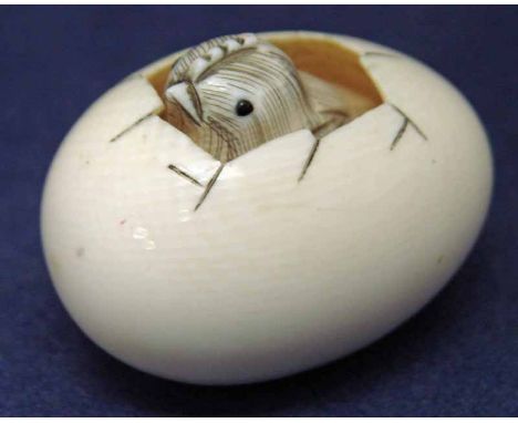 A Japanese carved ivory Netsuke as a Chick emerging from an Egg, chick carved separately and sits within the egg, red and bla