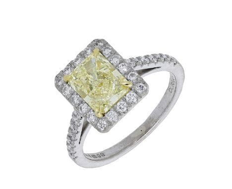 A diamond cluster ring, the cut-cornered Fancy Yellow diamond, weighing 1.57 carats, claw-set within a surround of brilliant-