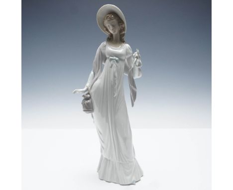 This early Lladro figurine, Dainty Lady, portrays a graceful woman in a flowing gown and broad-brimmed hat, holding a handker