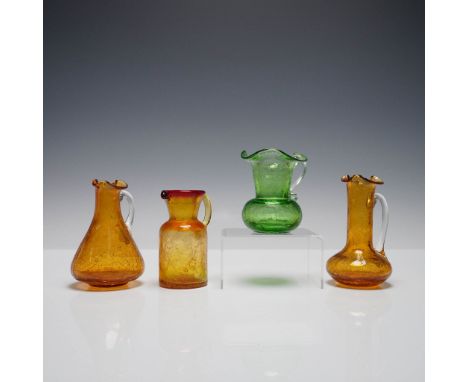 Set of four hand-blown crackle glass mini pitchers in amber, green, and amberina hues. Each pitcher features a unique silhoue