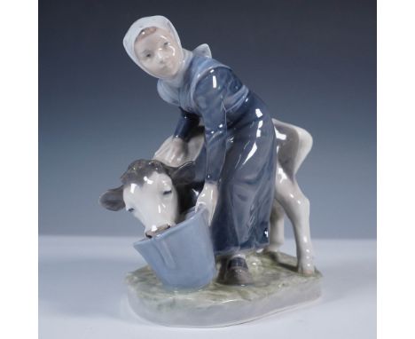 Crafted by the esteemed Royal Copenhagen of Denmark, this finely detailed porcelain figurine depicts a young girl feeding a c