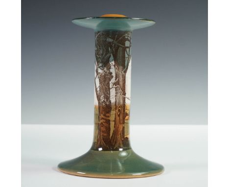 A ceramic candlestick holder with  transfer printed rural landscape with trees, cottages, and rolling hills under a cloudy sk