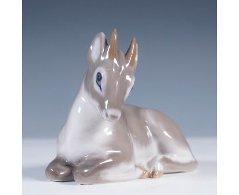This delicate porcelain figurine by Royal Copenhagen features a young fawn resting peacefully with its head turned back in a 