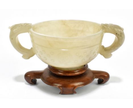 A Chinese carved and polished celadon jade twin handled cup, with central band of decoration to the body and spreading circul
