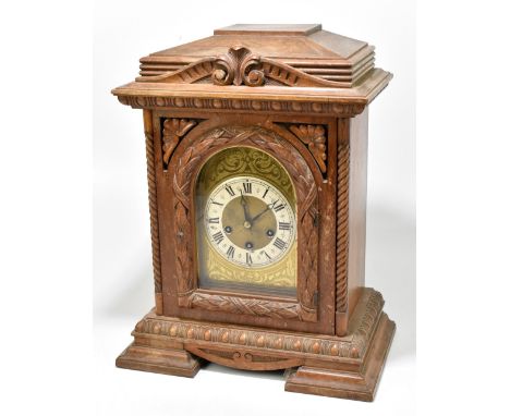 A large circa 1900 carved oak mantel clock with arched dial, Roman numerals to the silvered chapter ring and with eight day m