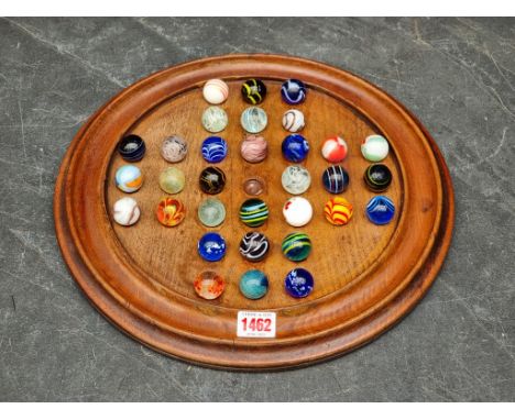 A mahogany solitaire board, 36cm diameter, with thirty two glass marbles, each approx 25mm diameter.