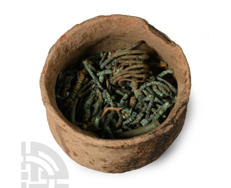 Circa 9th-11th century A.D. Comprising a quantity of bronze beads, dangles, coiled rings and other items, in a squat ceramic 