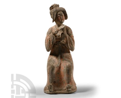 Tang Dynasty, 618-907 A.D. Seated on a low folding chair, with elaborately dressed hair and blusher on her cheeks, dressed in