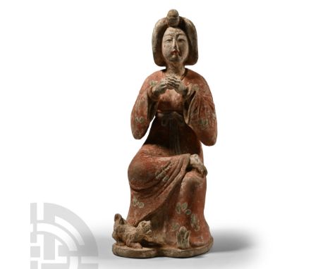 Tang Dynasty, 618-907 A.D. Sitting on a low folding chair, with elaborately dressed hair and blusher on her cheeks, wearing a