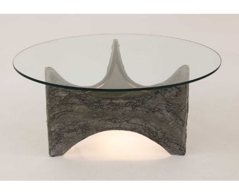 A brutalist coffee table,with a circular glass top, a cast aluminium plinth, with fitted lighting to the underneath of the ba