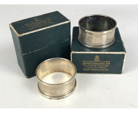 A pair of boxed George V silver napkin rings, each having engine-turned decoration surrounding a vacant cartouche, Henry Grif