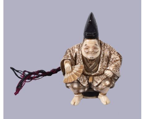 ϒ Shugyoku: A Japanese Ivory Netsuke, depicting a seated figure dressed in elaborate robes gold lacquered with karakusa and m