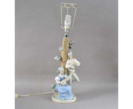 A Lladro porcelain table lamp, the column with two figures, the lady playing a lute on a naturalistic base, marked to the und