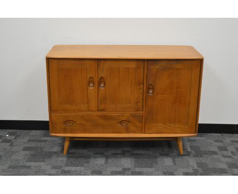 A 1960's/1970's elm Ercol sideboard,  two cupboard doors above a drawer, with one large cupboard door with Ercol label to the