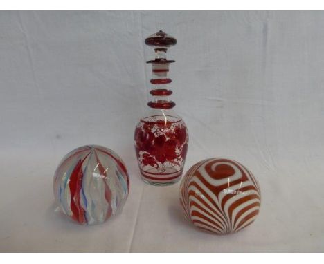 Two colourful glass paperweights and a Bohemian style garnet coloured glass decanter with stopper. 