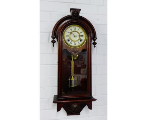 A mahogany wall clock, the arched top over an enamel chapter ring with Roman numerals, with glazed door, complete with pendul