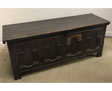 An 18th Century oak coffer, the later two plank top on replacement hinges over a four panel carved arch front on guilloche ca