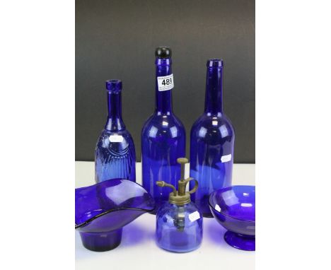 Two dark blue glass bowls, three similar bottles and an oil lamp.