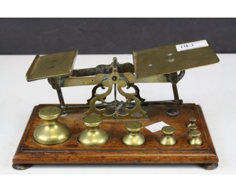 Set of Victorian brass postal scales with seven weights, raised on a mahogany base, 23cms wide 