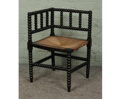 An Arts and Crafts ebonised bobbin turned corner chair, with rush seat.Hx62cmWx41cmDx41cm