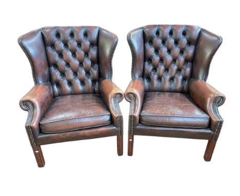 Pair brown leather button backed and brass studded wing armchairs, 96cm by 76cm by 75cm.