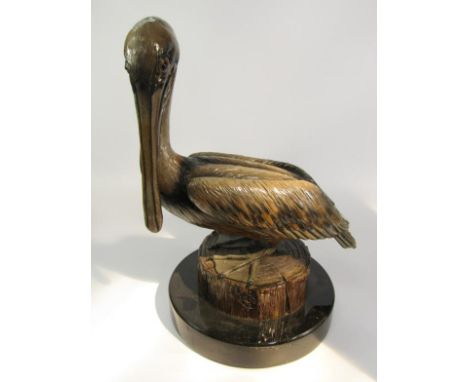 A pottery figure of a pelican perched on a tree trunk, raised on circular marble lazy susan, 50cm high.