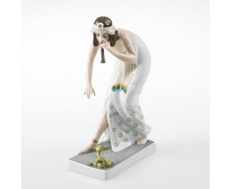 A ROSENTHAL FIGURE OF A SEMI-NUDE FEMALE SNAKE CHARMER, circa 1920,   bending down over a small green Cobra and playing a pip