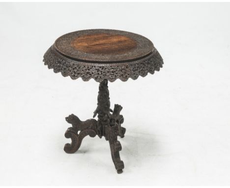 A CARVED BURMESE TILT TOP TRIPOD TABLE, the circular top with an ornate floral carved border and apron above a further heavil