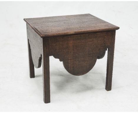 A GEORGE III OAK COMMODE, the hinged rectangular top over a scroll carved apron raised on square section legs continuing to f