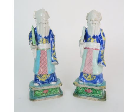 A PAIR OF CHINESE EXPORT MODELS OF OFFICIALS each standing and holding a scroll, diaper aprons and blue and yellow robes, on 