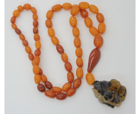 A STRING OF AMBER BEADS WITH A CHINESE CARVED PENDANT the agate pendant is carved with a bat, bee and moth among fruiting fol