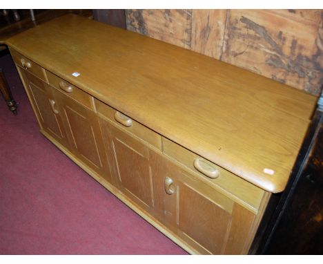 An Ercol type blond elm sideboard, having four frieze drawers over conforming twin hinged cupboard doors, on roller castors, 