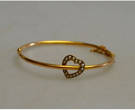 An antique hollow hinged yellow gold bangle with pearl set heart in centre