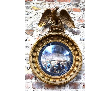 A giltwood and gesso convex mirror with ebonised reeded slip surmounted by a large carved giltwood spread eagle, 79 cm high x
