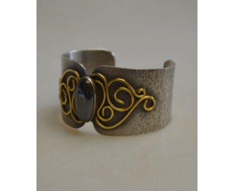 Carol Darby - a hammered silver bangle with gold scroll work having oval haematite in centre, London, 2007