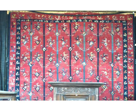 A large Bulgarian kilim carpet, early 20th century, the repeating stylised designs on mid-red ground, showing water damage/st