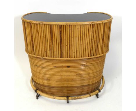 A 1970s bamboo freestanding kidney shaped bar, having a black laminate inset top, three open interior shelves, with lower bam