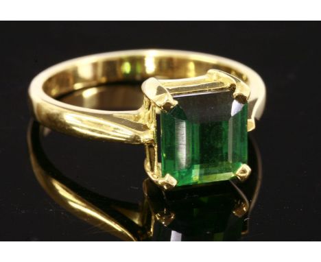 An 18ct gold single stone tourmaline ring,with an emerald cut green tourmaline, with a stepped pavilion, four claw set to a p