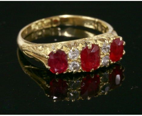 An 18ct gold, ruby and diamond carved head ring, c.1915,with three graduated oval mixed cut rubies, with pairs of Swiss cut d
