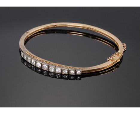 A cased Edwardian diamond set hinged bangle, c.1900,with a row of eleven graduated old European cut diamonds, all grain set t