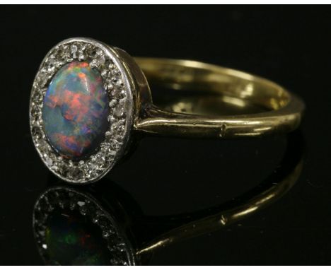 A black opal and diamond oval cluster ring, c.1915,with a central oval cabochon black opal, surrounded by a frame of eight cu