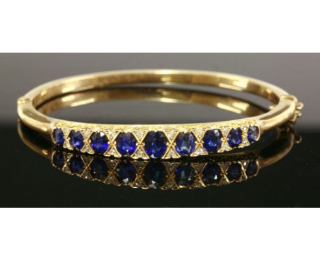 An Edwardian, sapphire and diamond, carved head style, hinged bangle, c.1910-1915,a centrepiece of graduated oval mixed cut s