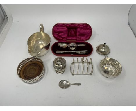 A silver coaster, sugar bowl, pepper pot, toast rack, caddy spoon, fork, spoon, and a napkin ring, various dates and marks 13