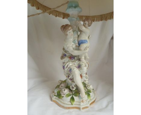 A German porcelain figural lamp base, in Meissen style, modeled as a seated woman supporting a small putto standing on her la