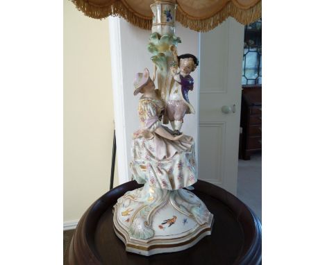 A German porcelain candle stick, probably Meissen, but outside decorated, modeled as a seated woman supporting a small boy st