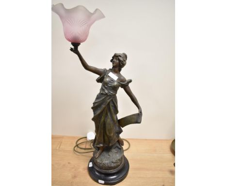 A vintage cast spelter table lamp with pink shade, in the form of a classically attired maiden with outstretched arms.