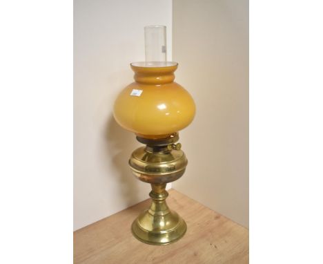 An early 20th Century oil lamp, having an amber coloured glass shade, chimney, and brass body, measuring 55cm tall