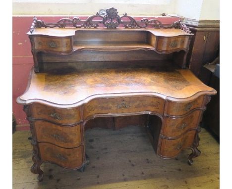 A burr walnut writing desk, having cross banded serpentine shaped front, with galleried shelf and drawers over a central door