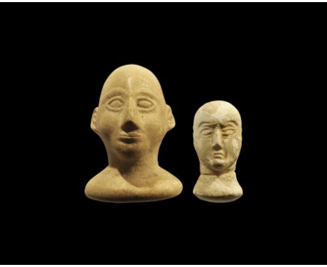 . A pair of carved undated archaistic stone heads comprising: one on discoid base with triangular nose and outlined lentoid e